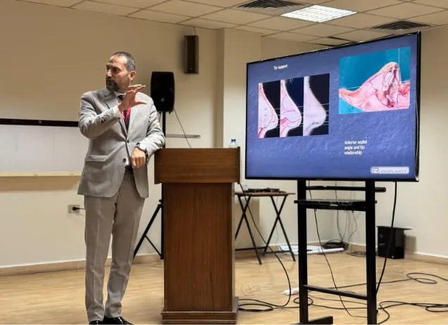 Dr Ali Khazzaal presenting beside a screen showing a rhinoplasty slide about tip support
